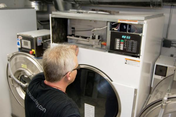 A laundry repair technician fixing a commercial washing machine.